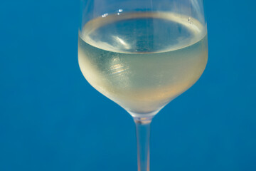 close-up of a wineglass filled with white wine by the blue water for celebration and romance