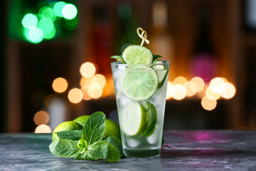 Glass of cold mojito on table against blurred lights