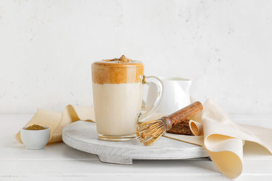 Glass cup of tasty dalgona hojicha latte and chasen on light background