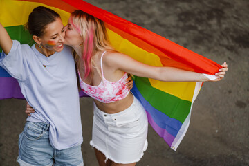 Fototapeta na wymiar Young lesbian couple walking with rainbow flags during pride parade