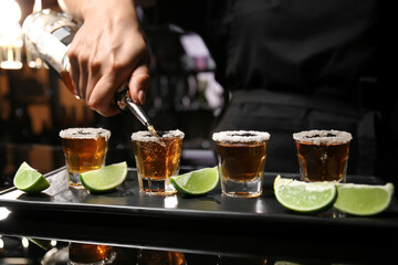 Bartender pouring tasty tequila into glasses at table in bar