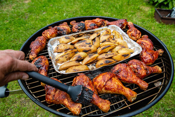Chicken legs and sliced potatoes baked on a grill - 457292772