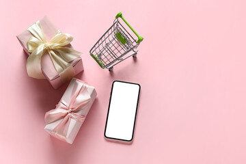 Shopping cart, phone and gift boxes on color background