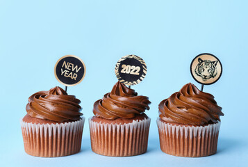 Tasty cupcakes for New Year 2022 celebration on color background