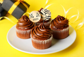 Plate with tasty cupcakes for New Year 2022 celebration on color background