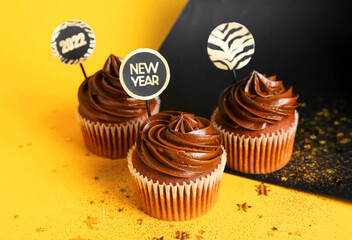 Tasty cupcakes for New Year 2022 celebration on color background