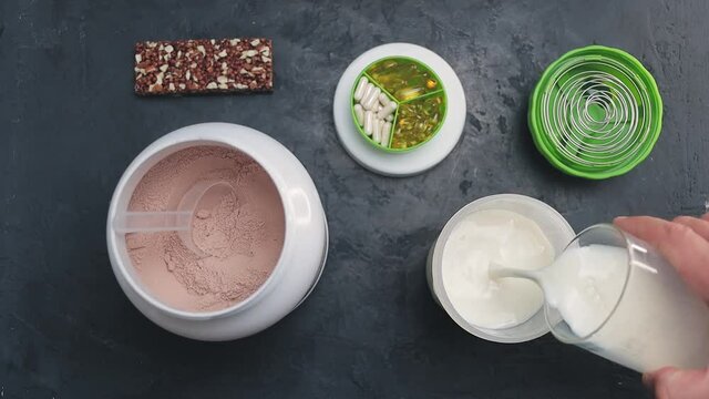 Pouring milk into shaker, process of making chocolate protein power drink, slow motion, top view