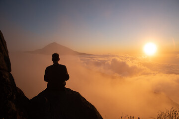 Boy looking at a sunset with the Teide volcano above the clouds and the sun hiding between them.