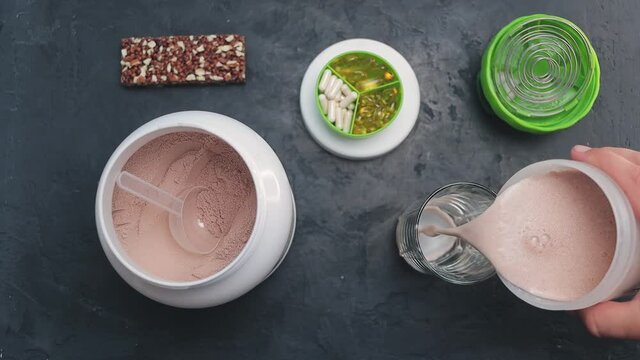 Pouring shaken chocolate whey protein drink or a smoothie into a glass, slow motion, top view