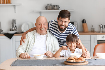 Happy man, his little son and father having breakfast in kitchen