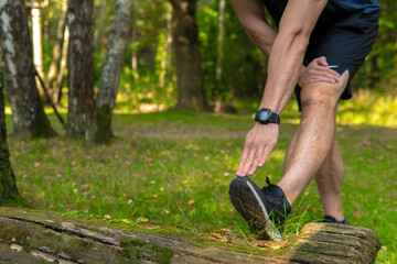 A young enduring athletic athlete is doing stretching in the forest outdoors, around the forest, oak trees. runner lifestyle jogger fit person marathon, park wellbeing. Summer running, feet stretches