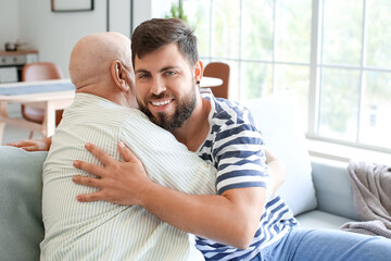 Happy man and his father hugging while sitting on sofa at home