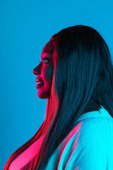 Portrait of African charming woman with long straight hair isolated on blue studio background in neon light. Concept of human emotions. Side view