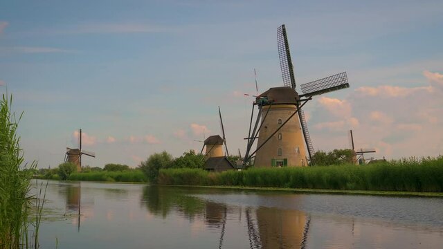 Pan right of historic windmills and a river at sunset in Kinderdijk, Netherlands. This system of 19 windmills was built around 1740 and is a UNESCO heritage site. 4K UHD video.