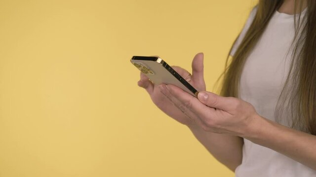 Female hands with smartphone on yellow background.