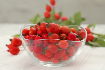 Ripe rose hip berries in bowl on white table, closeup