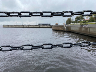 A river pier with chain-link fences in raindrops on the background of an urban landscape. Views of...