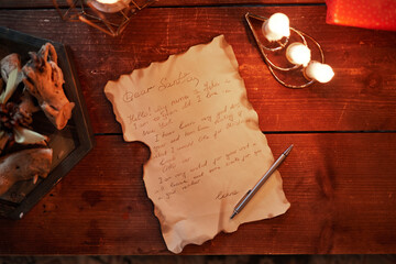 Directly above view of old letter with burnt edges, pen, candles on vintage wooden table