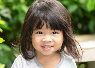 A headshot portrait of a cheerful baby Asian woman, a cute toddler little girl with adorable bangs hair, a child wearing a blue sweater smiling and looking to the camera.