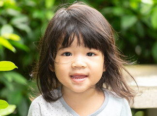 A headshot portrait of a cheerful baby Asian woman, a cute toddler little girl with adorable bangs hair, a child wearing a blue sweater smiling and looking to the camera.
