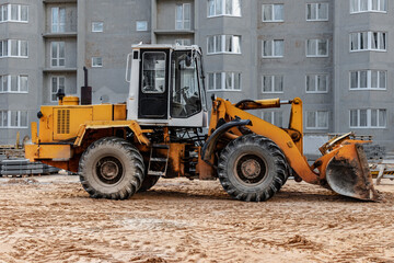 Obraz na płótnie Canvas Heavy wheel loader with a bucket at a construction site. Equipment for earthworks, transportation and loading of bulk materials - earth, sand, crushed stone.
