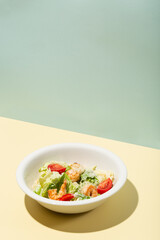 Caesar salad with shrimp in white plate on yellow hard shadow modern