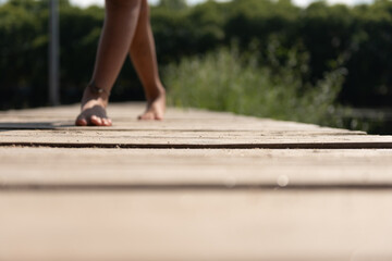 woman legs walking on a floating wooden dock in the river, followed by a boy.