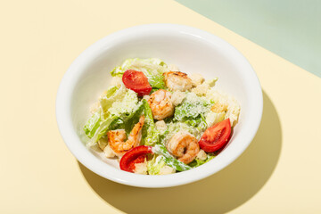 Caesar salad with shrimp in white plate on yellow hard shadow modern