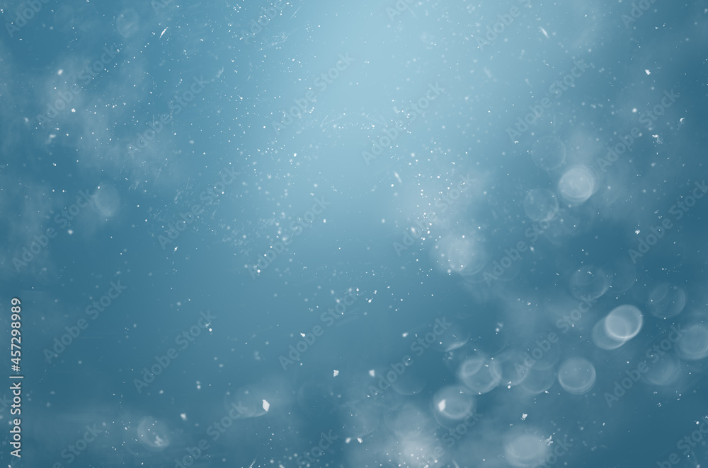 Wall mural blurred abstract background with bokeh and snowflakes in the air on a blue background