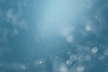 blurred abstract background with bokeh and snowflakes in the air on a blue background