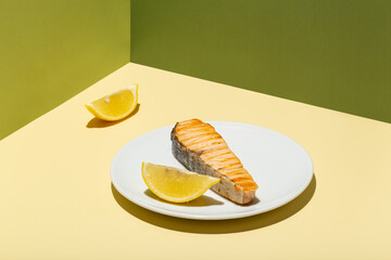 Baked salmon fillet with lemon on white plate hard modern shadow green background