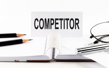 Text COMPETITOR on paper card,pen, pencils, glasses,financial documentation on table - business concept