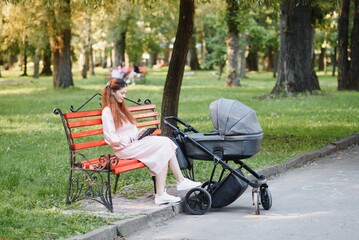 Mum sitting on a bench. Woman pushing her toddler sitting in a pram. Lady with a tablet.