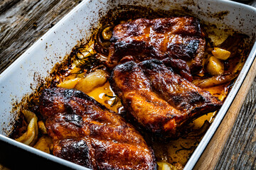 Tasty roasted ribs with onion and garlic served on frying pan on wooden table

