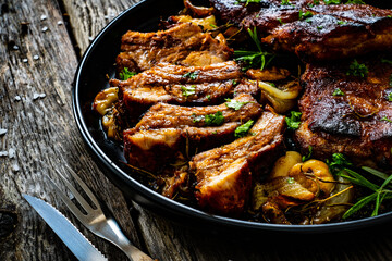 Tasty roasted ribs with onion and garlic on wooden table
