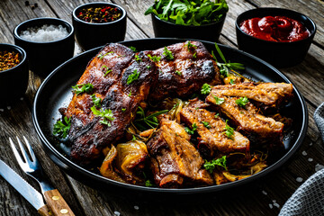 Tasty roasted ribs with onion and garlic on wooden table
