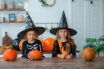 two little girls in witch costumes in the kitchen are playing with balloons for the Halloween holiday