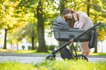 family, child and parenthood concept - happy mother walking with baby stroller in park.