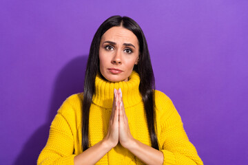 Portrait of young pleading girl arms palms together look camera sullen face isolated on purple...