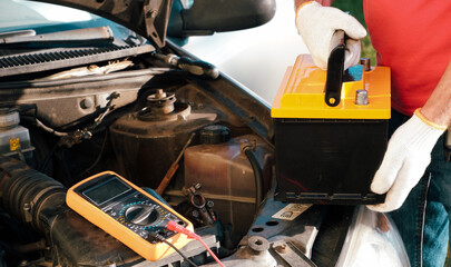 Car maintenance before winter. An auto mechanic is changing the car battery. View of the hands with the battery when installing a new battery.