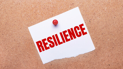 White paper with the text RESILIENCE is attached to the wooden background with a red button.