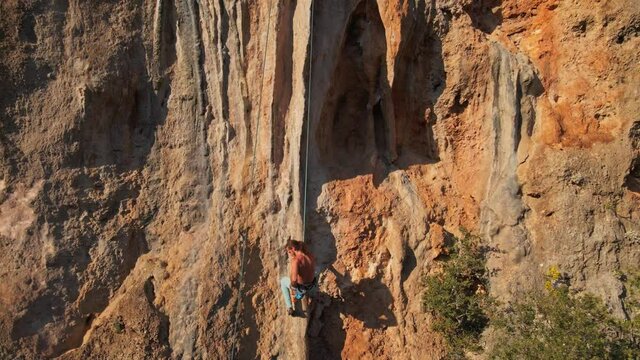 slow motion footage of man rock climber with long hair hanging on rope and going down after successful ascent of challenging route on limestone cliff.