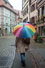 Portrait on back view of woman with a rainbow umbrella walking in the street