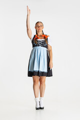 Full-length portrait of beautiful woman, waitress in traditional Austrian or Bavarian costume standing alone isolated over white background.