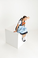 Attractive Caucasian woman, waitress in traditional Austrian or Bavarian costume sitting on huge box isolated over white background. Oktoberfest concept