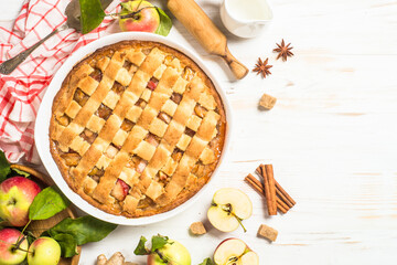 Apple pie with ginger and cinnamon at white wooden table with ingredients for cooking. Top view image with copy space.