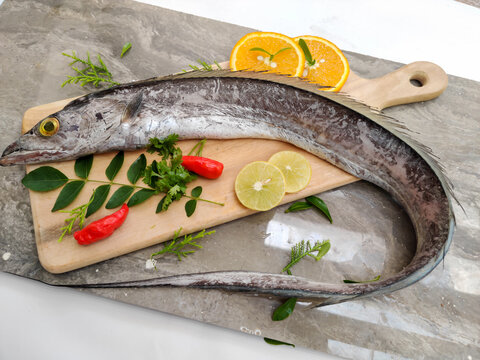 Fresh Largehead hairtail fish,Belt fish decorated with herbs and vegetables on a wooden pad.Selective focus.