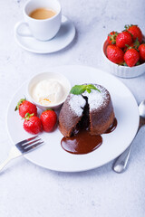 Lava cake - chocolate fondant cake with vanilla ice cream, strawberries, mint and coffee. Traditional French pastries. Close-up, selective focus.