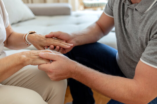 Cropped shot of an unrecognizable male nurse holding his senior patient's hand in comfort. Mother and son hands holding together in love and support after losing loved ones amid coronavirus outbreak.