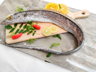 Fresh Largehead hairtail fish,Belt fish decorated with herbs and vegetables on a wooden pad.Selective focus.